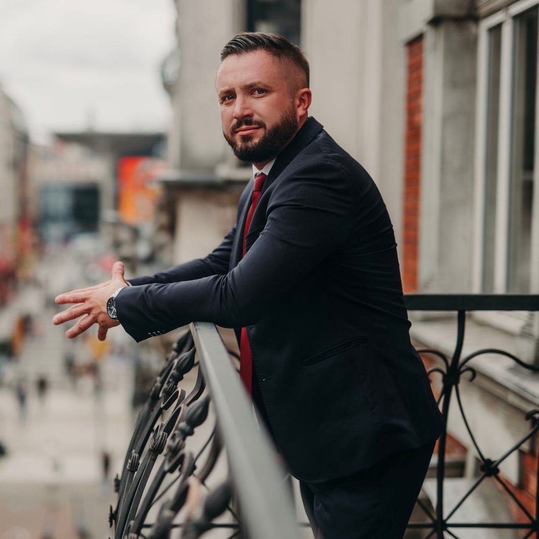 Robert Rał w granatowym garniturze na balkonie
